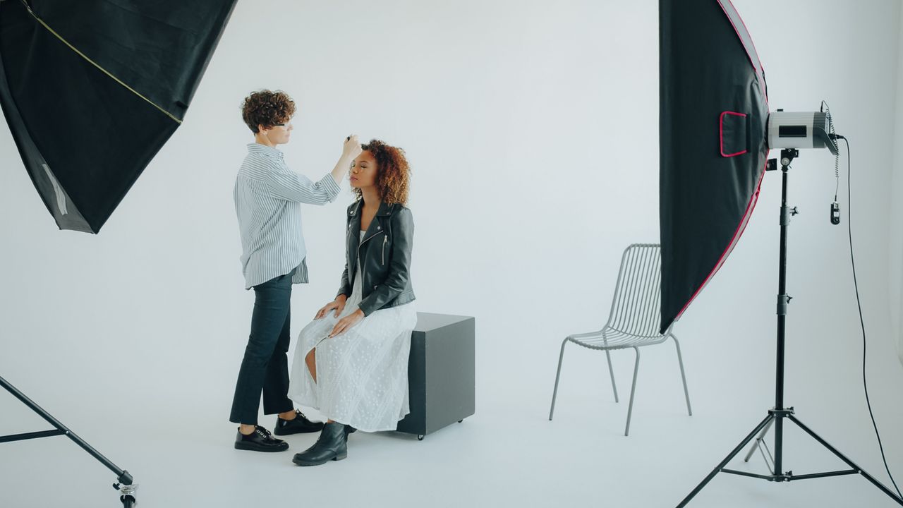 Makeup artist preparing model in a photography studio setup.